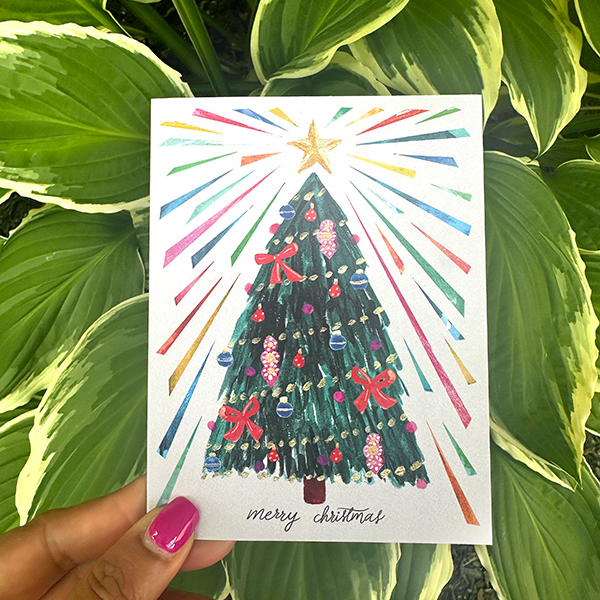 a hand holding a card with a christmas tree on it