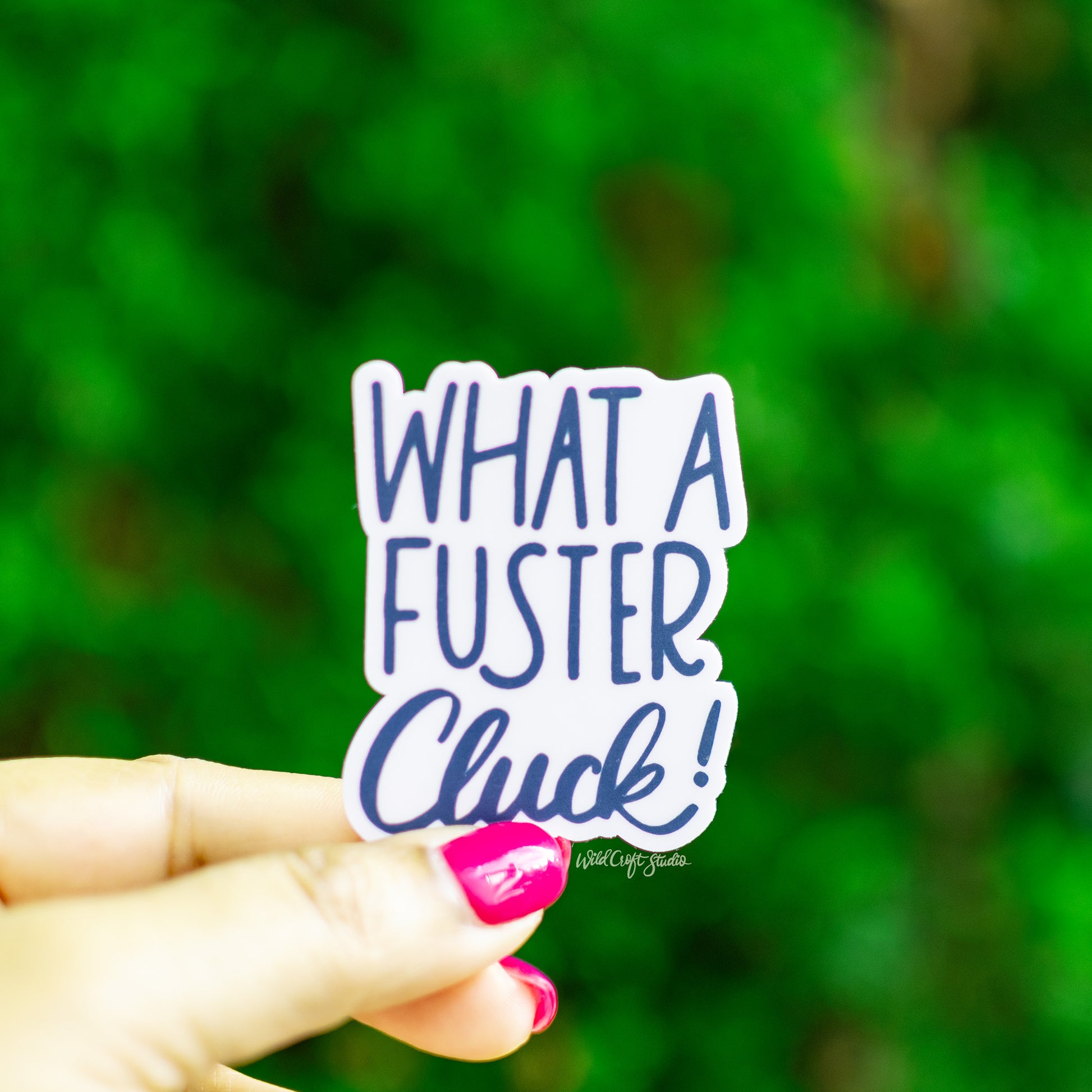 a person holding a sticker that says what a fuster click