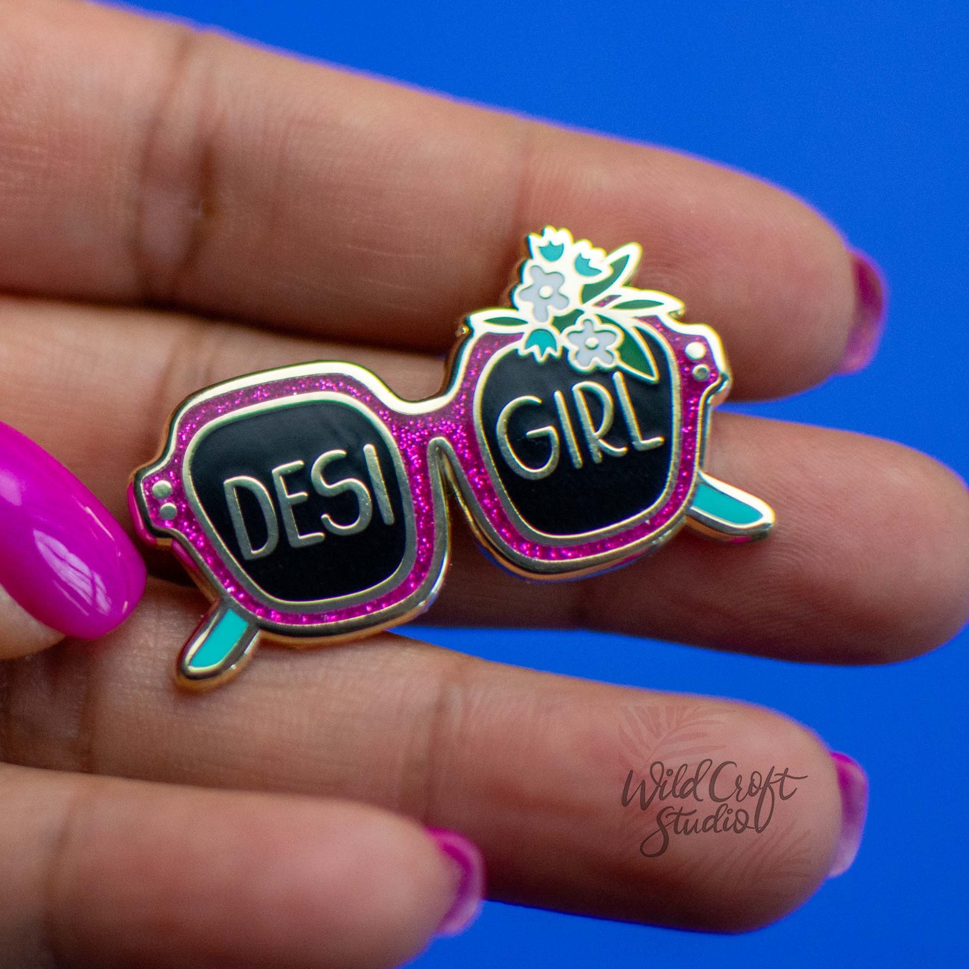 a hand holding a pink and black pin with a desi girl on it